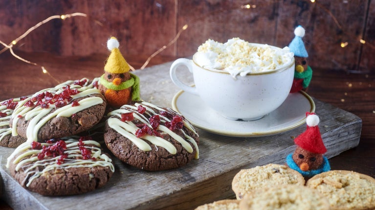A toothsome trio of crumble-topped mince pie, luxury hot chocolate, and Christmas cookie with felted robins in bobble hats peeping round the dishes